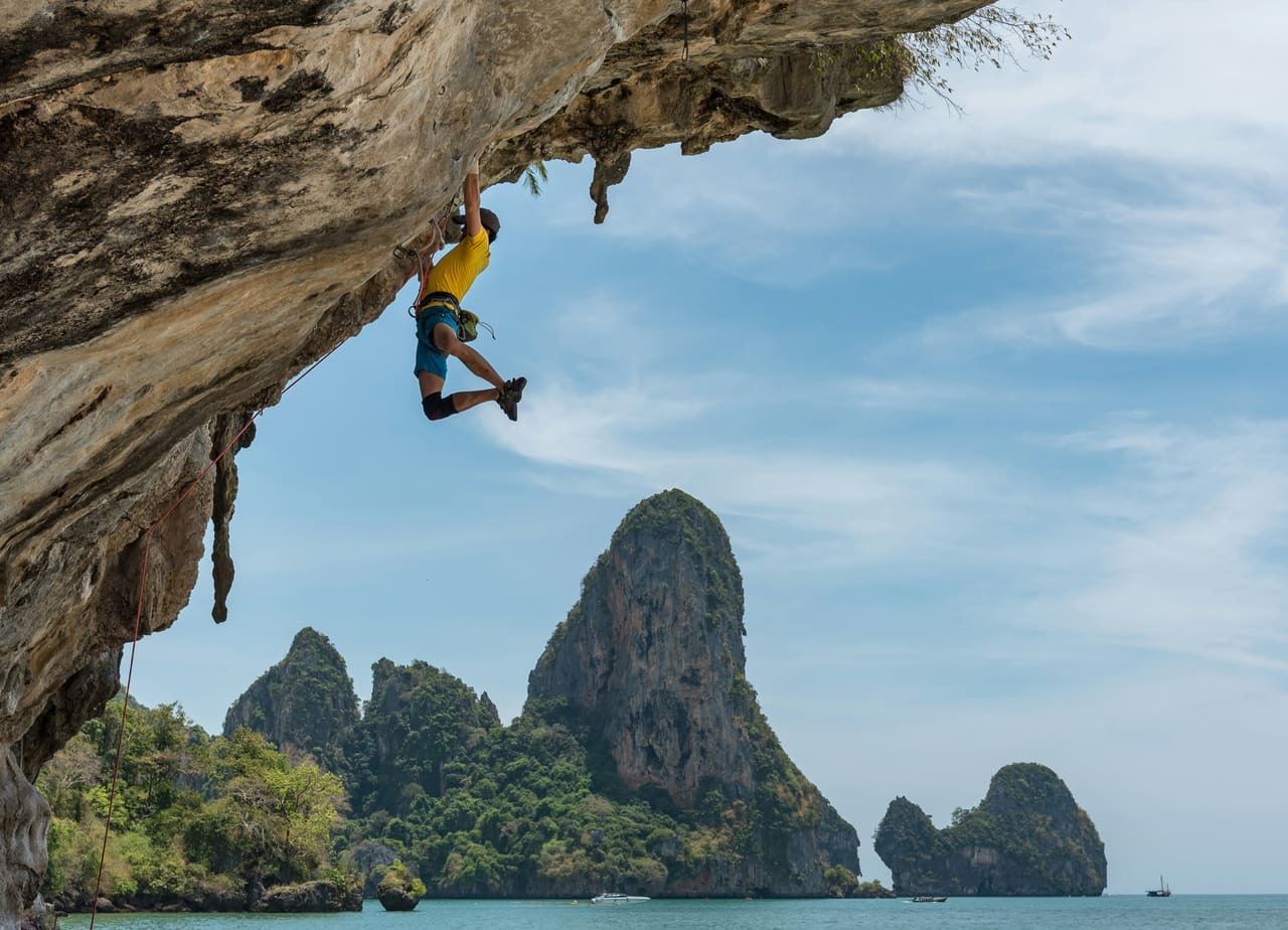 Rock climber ascending a steep seaside cliff — the kind of active, pain-free movement effective pain management can restore